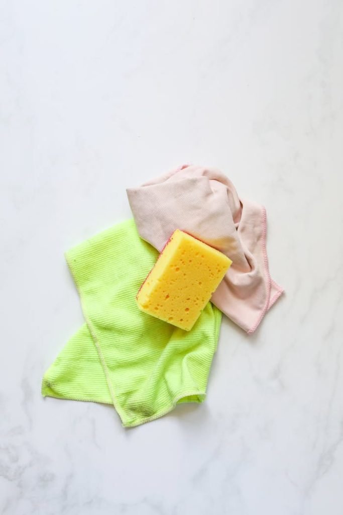 Colorful cleaning supplies with sponge on a marble surface, ideal for housekeeping themes.