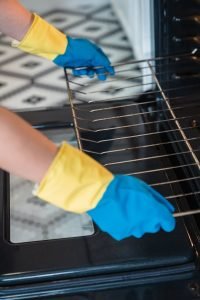 Person wearing gloves cleaning an oven, focusing on hygiene and household chores.